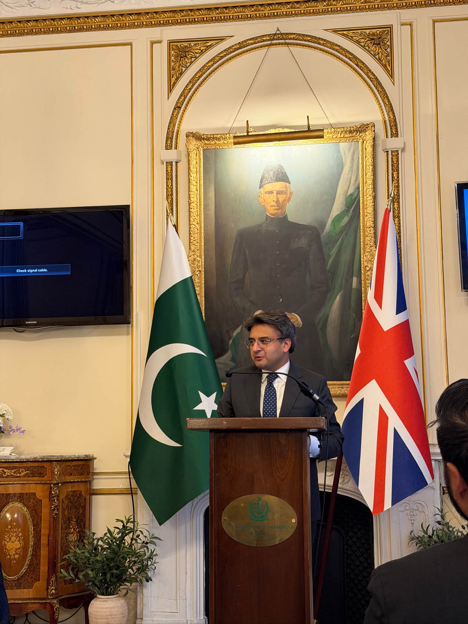 Speaker at a podium between the flags of Pakistan and the United Kingdom during the youth engagement session at the Pakistan High Commission in London